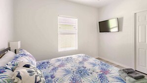 Een slaapkamer met een bed, een aan de muur bevestigde televisie en een raam met zonwering.