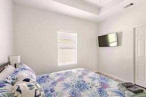 A bedroom with a bed, a TV mounted on the wall, and a window with blinds. - Beachfront, Views, 3bdr 2bth - The Bleu Pearl (Bolivar Peninsula)