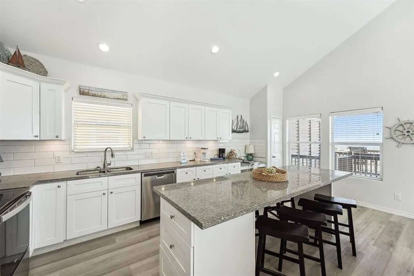 A modern kitchen with white cabinetry, a granite countertop, and a bar area with stools.