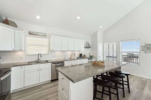 A modern kitchen with white cabinetry, a granite countertop, and a bar area with stools. - Beachfront, Views, 3bdr 2bth - The Bleu Pearl (Bolivar Peninsula)