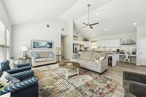 A spacious living area with a sofa, coffee table, and a rug. There is a kitchen with white cabinets and a dining area. - Beachfront, Views, 3bdr 2bth - The Bleu Pearl (Bolivar Peninsula)