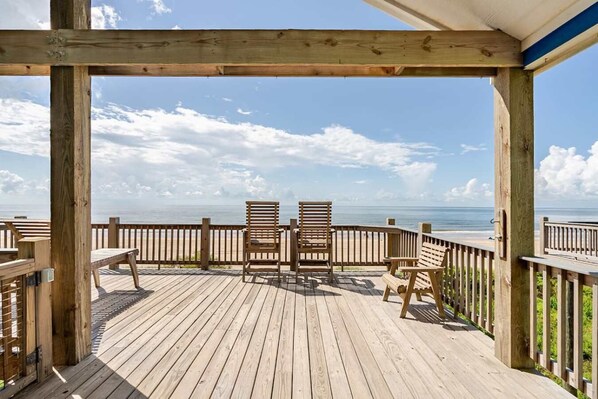 Une terrasse en bois avec deux chaises et une table, donnant sur une plage.