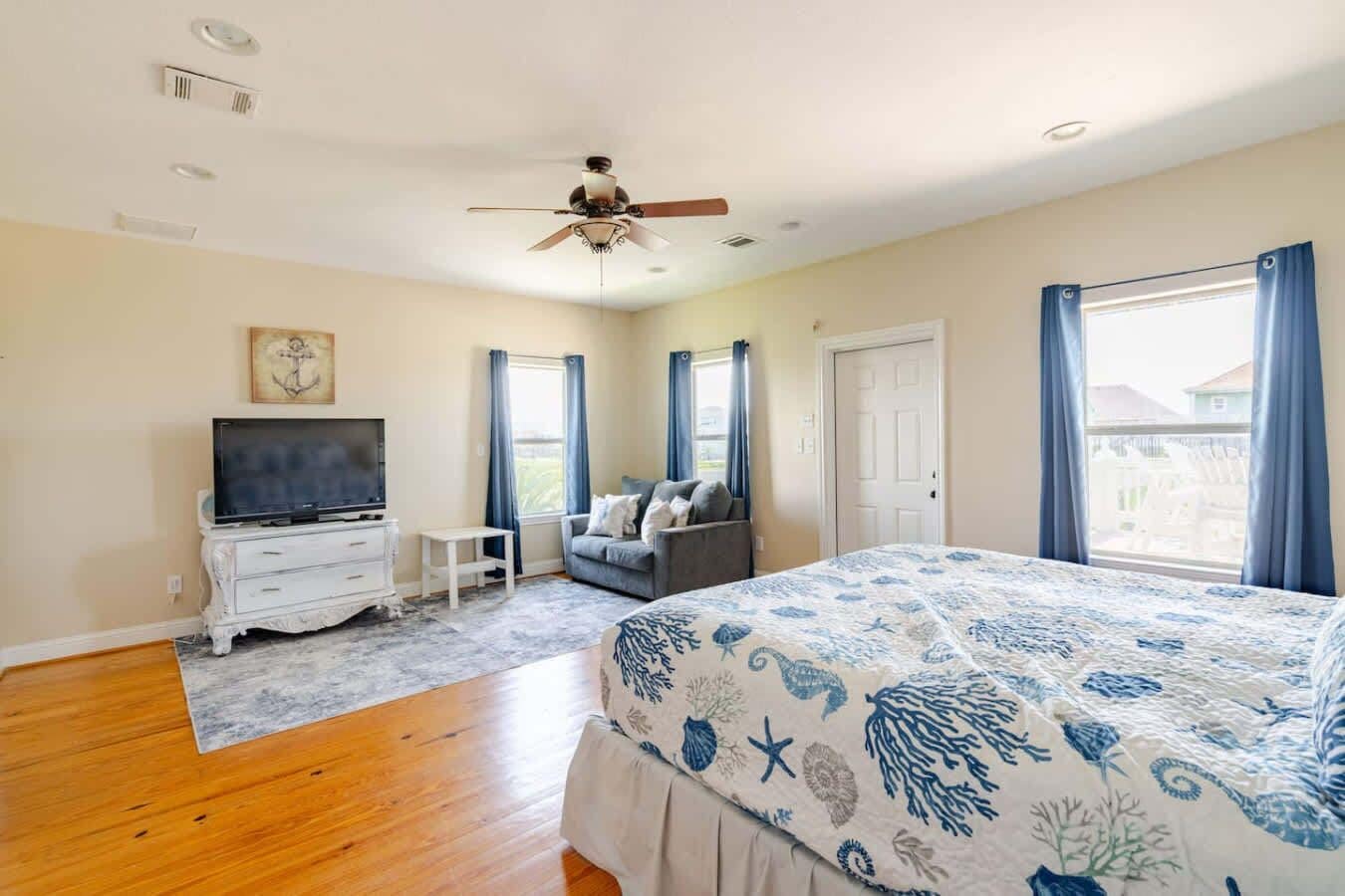 A bedroom with a bed, a television, a sofa, and a ceiling fan.