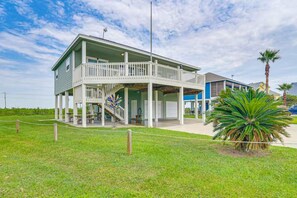 A two-story building with a balcony, a staircase, and a fenced area with a palm tree. - Family Retreat, Hangout Garage & Fire Pit, 3Bd 2Bth (Bolivar Peninsula)