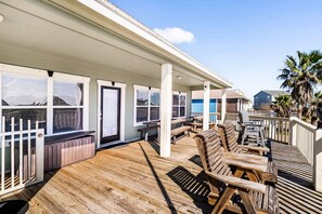 A wooden deck with outdoor seating, a covered area with windows, and a view of the ocean. - Family Retreat, Hangout Garage & Fire Pit, 3Bd 2Bth (Bolivar Peninsula)