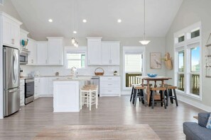 A modern kitchen with white cabinets, a central island, and a dining area with a wooden table and chairs. - 3 Bdr 3 Bth, King Bed, No Fees (Bolivar Peninsula)
