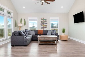 A spacious living room with a sectional sofa, a coffee table, a ceiling fan, and a flat-screen TV mounted on the wall. - 3 Bdr 3 Bth, King Bed, No Fees (Bolivar Peninsula)