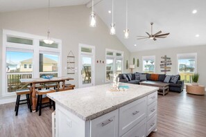 A spacious kitchen with a large island, a dining area with wooden chairs, a dark-colored sofa, and a ceiling fan. - 3 Bdr 3 Bth, King Bed, No Fees (Bolivar Peninsula)