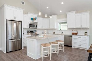 A modern kitchen with white cabinetry, stainless steel appliances, and a central island with bar stools. - 3 Bdr 3 Bth, King Bed, No Fees (Bolivar Peninsula)