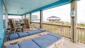 A covered outdoor area with wooden benches and a table, overlooking a beach and buildings. - Gulf Views, Steps to Beach, 2 King Beds, 3Bd 2Bth (Bolivar Peninsula)