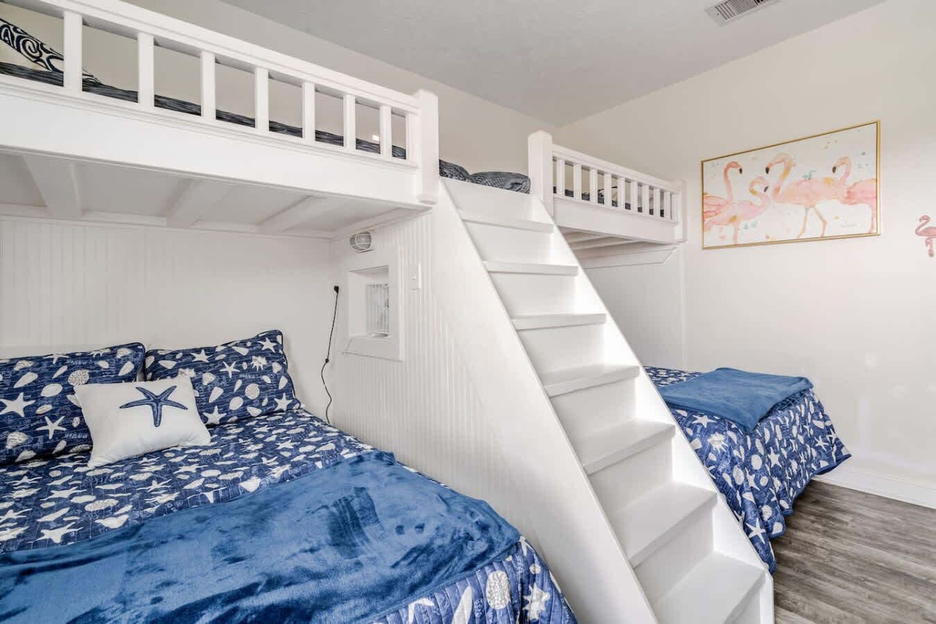 A room with bunk beds, a staircase, and a painting of flamingos.