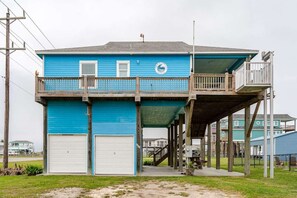 Ein zweistöckiges Gebäude mit blauer Fassade, einem Balkon im oberen Stockwerk und einer Garage im unteren Stockwerk.