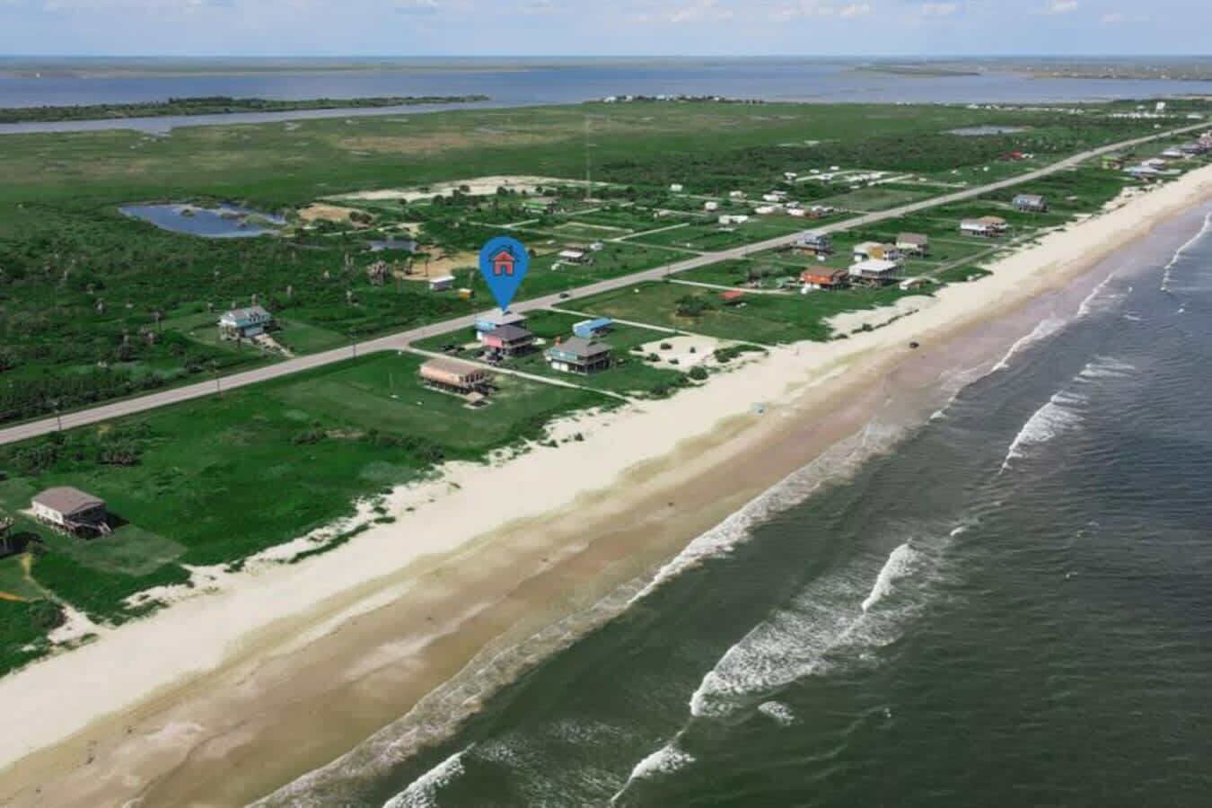 An aerial view of a coastal area with a beach, houses, and a road.