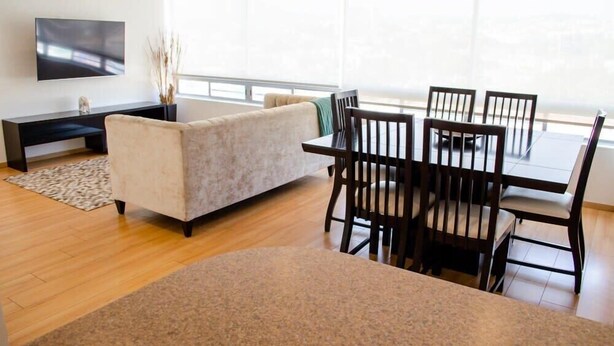 A modern living room with a sofa, dining table, chairs, a flat-screen TV, and a large window. - Capitalia  Bright & Cozy Family Apt in Santa Fe (Ciudad de México)