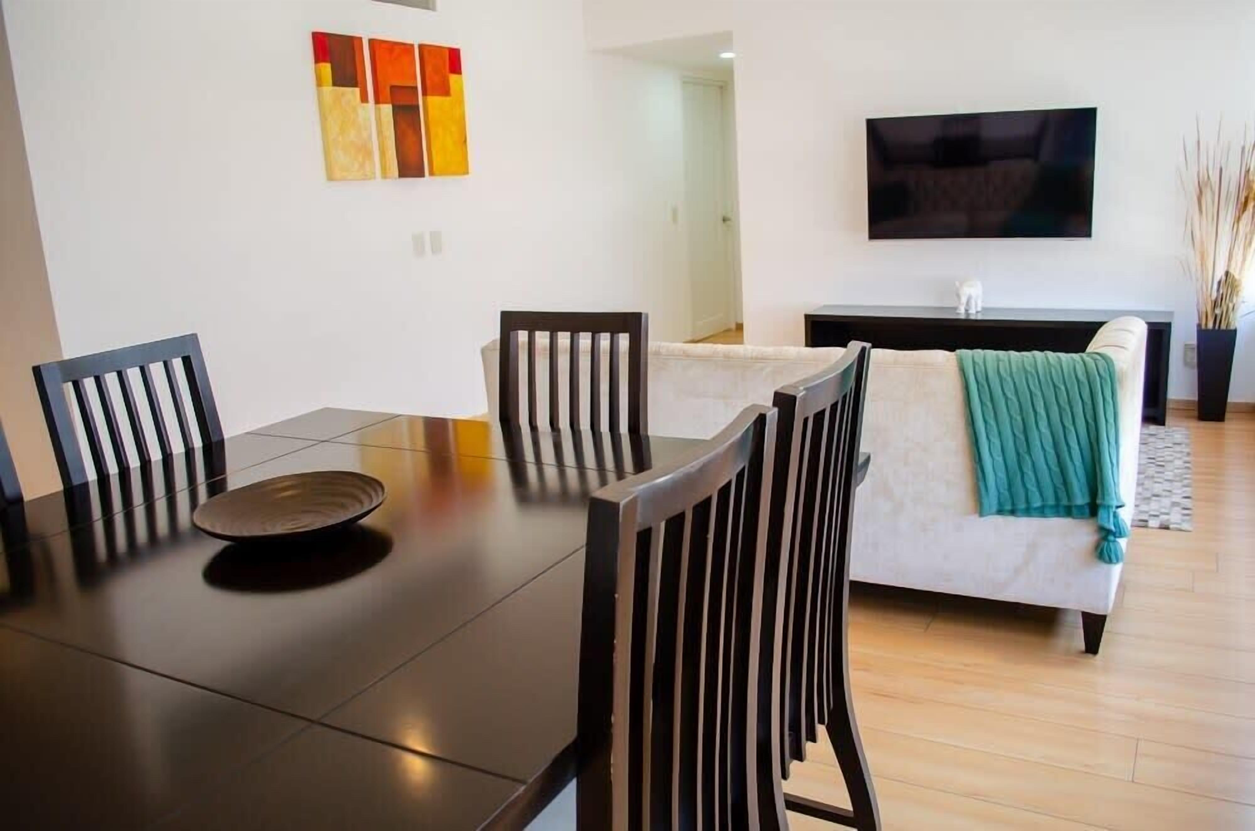 A dining area with a table, chairs, a sofa, a TV, and abstract art on the wall.