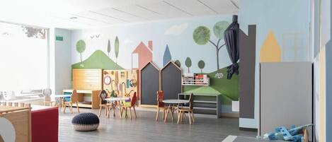 Une salle de jeux pour enfants avec une fresque murale, des meubles en bois et un espace de jeu rouge.