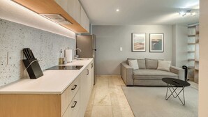 A modern kitchen with a countertop, sink, and cabinets, a living area with a sofa and a coffee table, and a bookshelf. - Modern King Studio in Central Roma Norte (Ciudad de México)