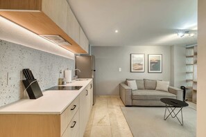 A modern kitchen with a countertop, sink, and cabinets, a living area with a sofa and a coffee table, and a bookshelf. - Modern King Studio in Central Roma Norte (Ciudad de México)
