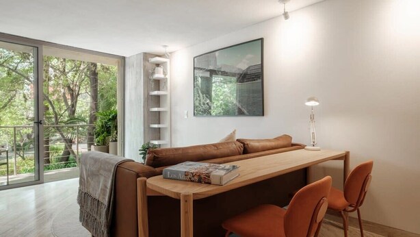 A modern living space with a wooden table, brown sofa, and orange chairs. - Modern Loft with Balcony & View of Parque Mexico (Ciudad de México)