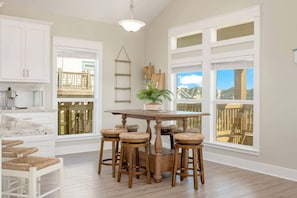 A kitchen with a wooden table and stools, a hanging light fixture, and large windows with a view of a fence and buildings. - 3 Bd 2 5 Bth, King Bed, Pet Friendly (Bolivar Peninsula)