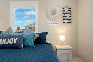 A bedroom with a bed, pillows, a nightstand, a lamp, a wall sign, and a decorative mirror. - 3 Bd 2 5 Bth, King Bed, Pet Friendly (Bolivar Peninsula)
