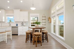 A kitchen with white cabinetry, a central island with stools, and a view through large windows. - 3 Bd 2 5 Bth, King Bed, Pet Friendly (Bolivar Peninsula)