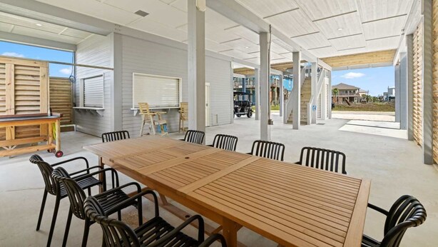 An open-plan dining area with a long wooden table and chairs, a white ceiling, and a view of the outside. - Golf Cart, Elevator, Stylish, 12 guests - LaPerla (Bolivar Peninsula)