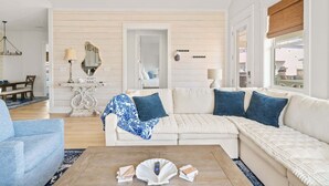 A living room with a sectional sofa, a coffee table, and a dining area with a table and chairs. - Golf Cart, Elevator, Stylish, 12 guests - LaPerla (Bolivar Peninsula)