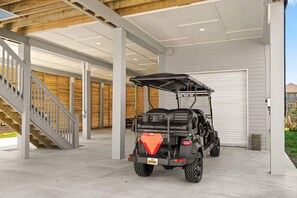 Ein überdachter Parkbereich mit Golfwagen, Betonboden und einer Treppe.