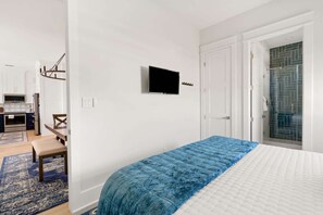 Ein Schlafzimmer mit Bett, Fernseher, Tür und Duschbereich.