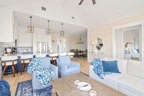 A modern living room with a sofa, chairs, a coffee table, and a kitchen area with a dining table. - Golf Cart, Elevator, Stylish, 12 guests - LaPerla (Bolivar Peninsula)