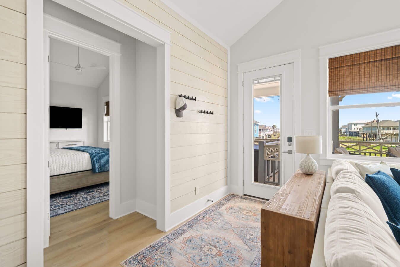 Une chambre avec un lit, une télévision, un mur en bois, un balcon et une vue sur des maisons.