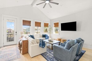 A spacious living room with a high ceiling, a ceiling fan, a large window with a view, a flat-screen TV mounted on the wall, and a seating area with a sofa and armchairs. - Golf Cart, Elevator, Stylish, 12 guests - LaPerla (Bolivar Peninsula)
