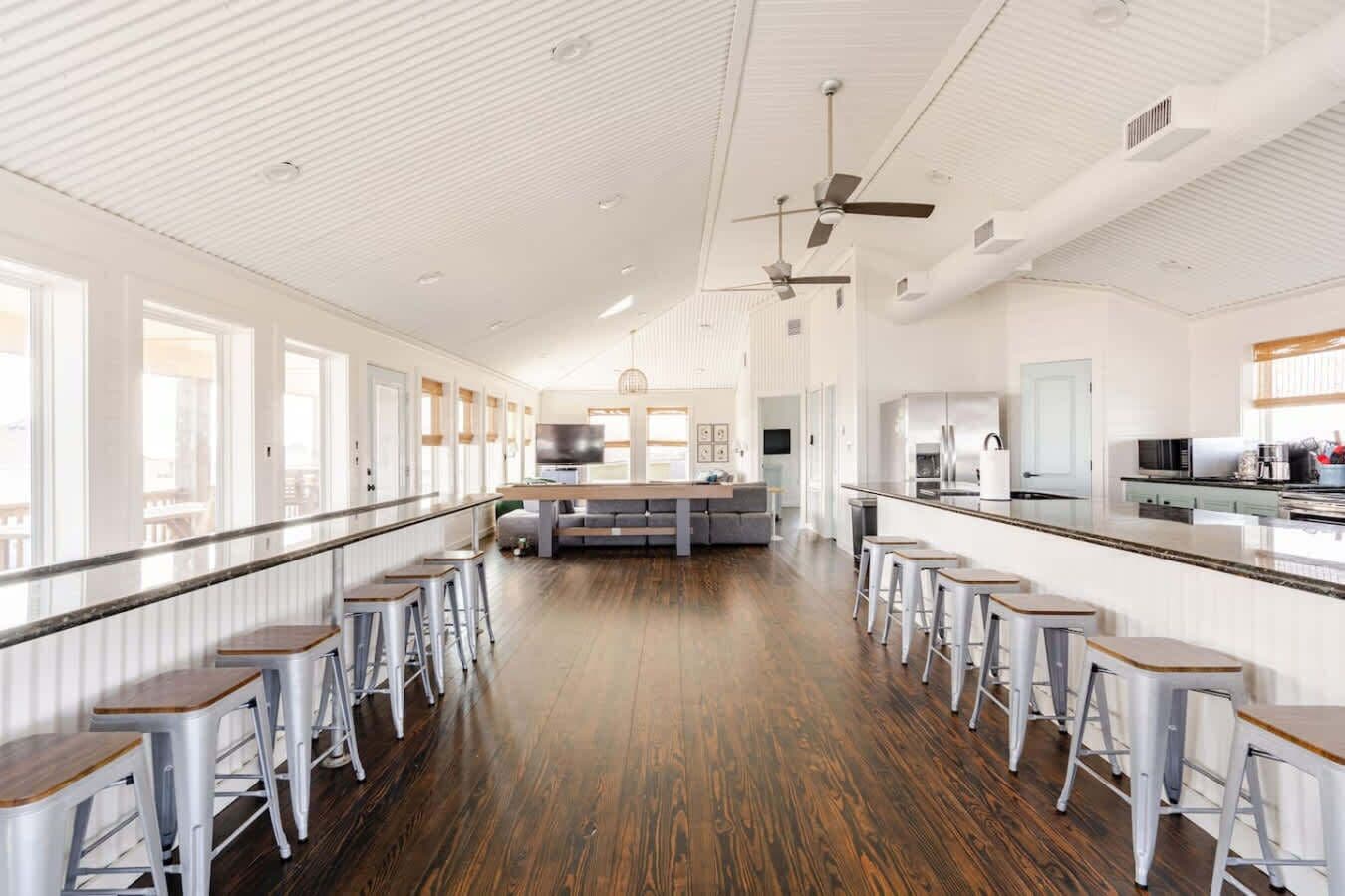 A spacious room with a long counter, bar stools, a central seating area, and a kitchen.