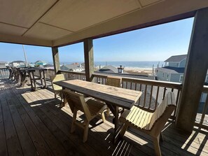 Un terrazza in legno con tavolo e sedie, con vista sulla spiaggia e sull'oceano.