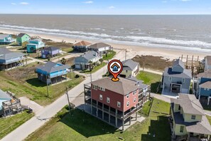 A coastal residential area with a prominent red building, surrounded by other houses, a beach, and the ocean. - 6BR 3Bth Beach House Game Deck, Grill, 26 Guests (Bolivar Peninsula)