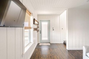 A hallway with wooden floors, a door, and a window with blinds. - 6BR 3Bth Beach House Game Deck, Grill, 26 Guests (Bolivar Peninsula)