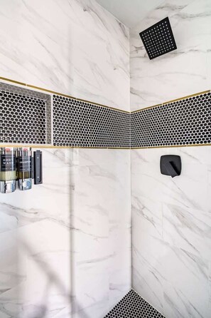 A bathroom with a white marble wall, a black and white patterned shower area, and a shelf with toiletries. - Unit B of Crystal Beach's Premier Triplex 2Bd 1Bth (Bolivar Peninsula)