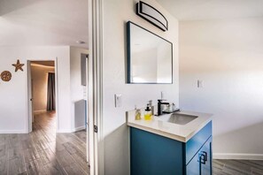 Une salle de bain moderne avec un grand miroir, un lavabo surmonté d’un meuble bleu et un plancher en bois.