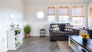A living room with a grey sofa, a white shelving unit, and a wooden coffee table. - Big 6BR Beach Getaway for 20 Near Ferry, 3 Units (Bolivar Peninsula)