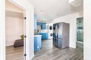 A modern kitchen with a stainless steel refrigerator, a washing machine, and blue cabinets. - Big 6BR Beach Getaway for 20 Near Ferry, 3 Units (Bolivar Peninsula)