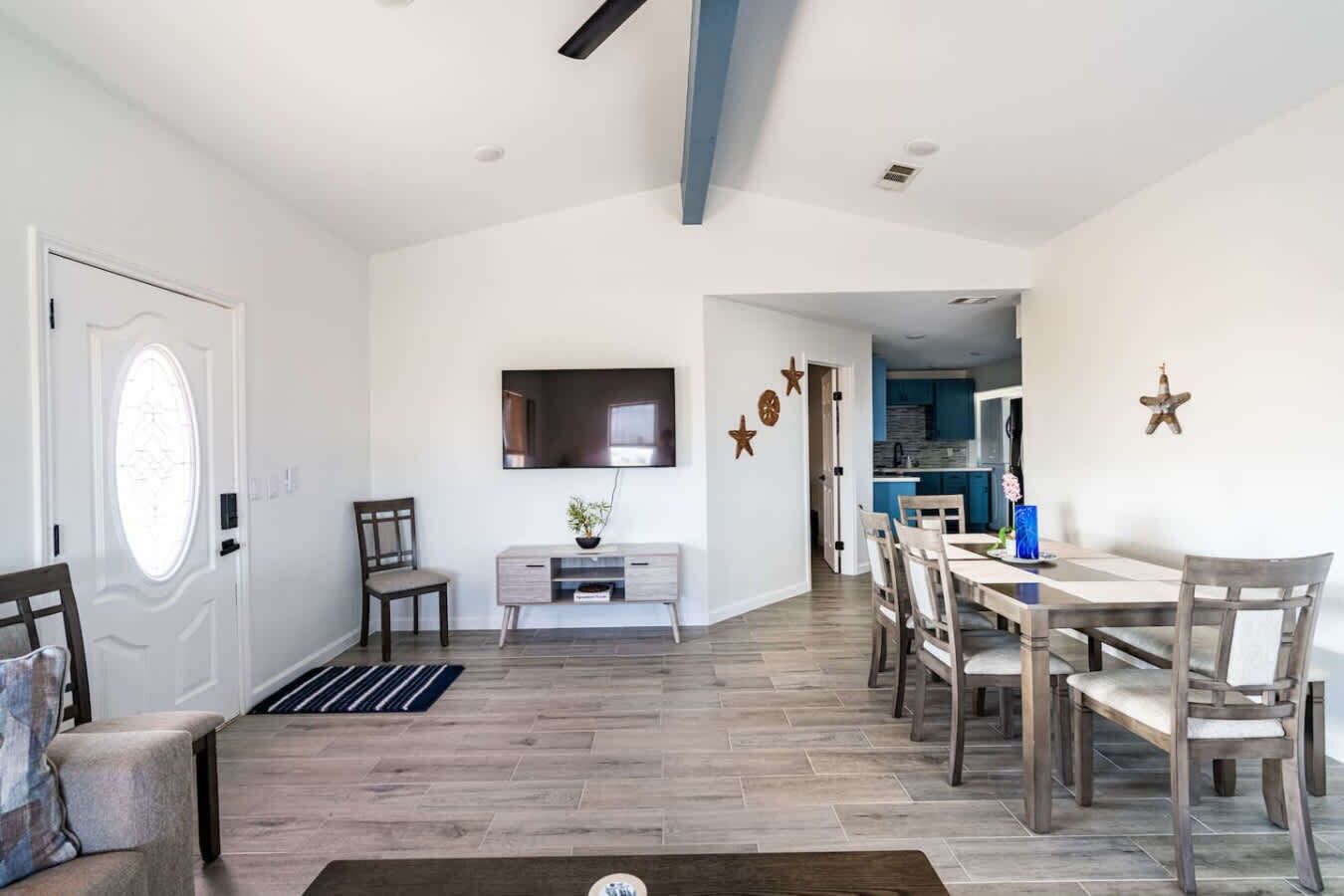 A spacious living area with a dining table, chairs, a TV, and a kitchen in the background.