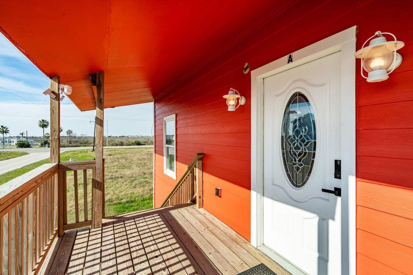Un porche avec une balustrade en bois, une porte blanche dotée d’une vitre et un mur extérieur rouge.