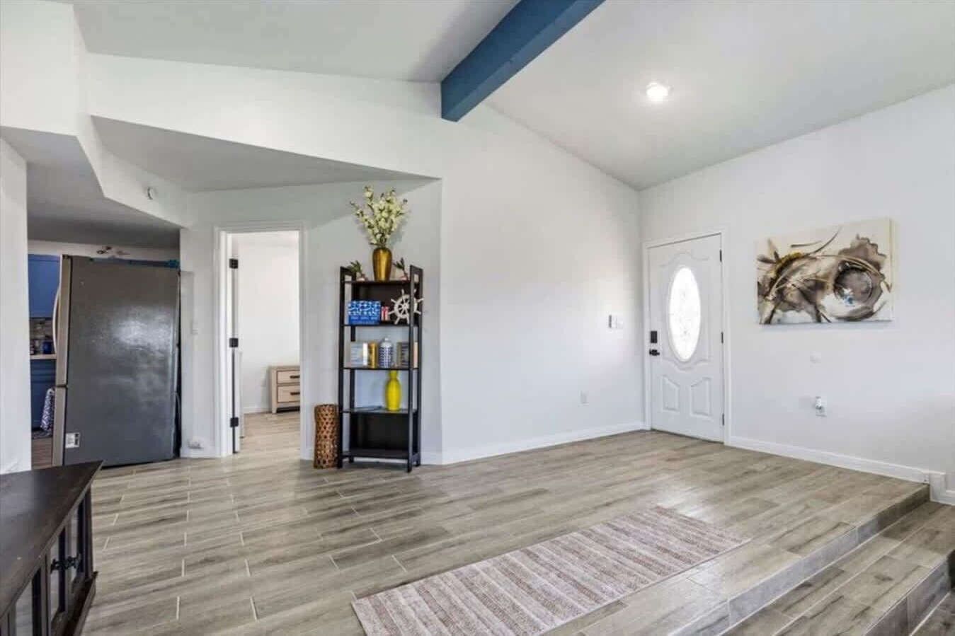 A spacious room with a wooden floor, a bookshelf, a door, and a wall-mounted artwork.