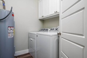 A laundry room with a washer and dryer, a water heater, and white cabinets above. - 1 King, 4 Queens, Pet-Friendly (Bolivar Peninsula)