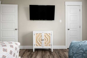 A bedroom with a bed, a TV mounted on the wall, a cabinet, and two doors. - 1 King, 4 Queens, Pet-Friendly (Bolivar Peninsula)