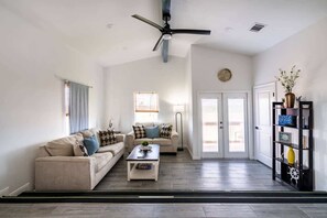A spacious living room with a high ceiling, a ceiling fan, a sofa set, a coffee table, a bookshelf, and a door leading to an outdoor area. - Unit A of Crystal Beach's Premier Triplex 2Bd 1Bth (Bolivar Peninsula)