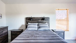 Een slaapkamer met een bed, twee nachtkastjes, een dressoir en een raam met uitzicht.