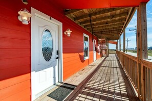 A covered porch with a wooden railing, a door with a glass panel, and a view of the outside. - Unit A of Crystal Beach's Premier Triplex 2Bd 1Bth (Bolivar Peninsula)