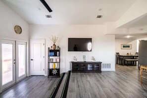 A spacious living room with a flat-screen TV, a bookshelf, and a dining area with a table and chairs. - Unit A of Crystal Beach's Premier Triplex 2Bd 1Bth (Bolivar Peninsula)